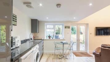 A modern kitchen with a washing machine, a coffee maker, and a dining area with a table and chairs.