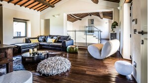 Ein geräumiges Wohnzimmer mit hoher Holzbalkendecke, einer schwarzen Ledersofa, einem weißen Sessel und einem Couchtisch mit Dekoration.