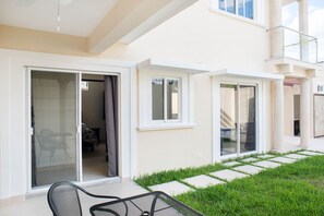 A modern building with large sliding glass doors, a covered outdoor seating area, and a well-maintained lawn.
