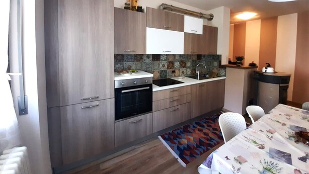 Cozinha moderna com armários de madeira, forno embutido e uma pia. Há uma área de jantar com mesa e cadeiras.