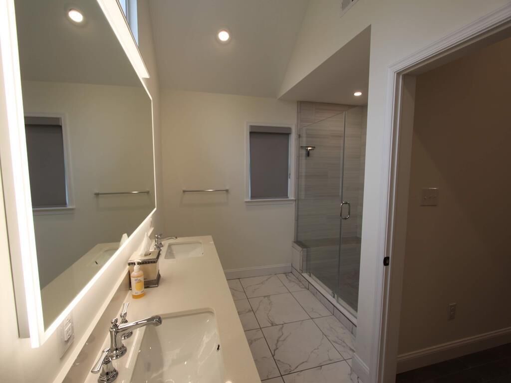 Un baño moderno con un espejo grande, lavamanos doble y cabina de ducha de vidrio.