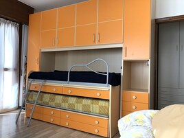 Un dormitorio con literas, un armario naranja y un escritorio pequeño.