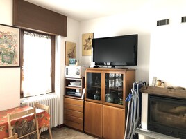 Una sala de estar con televisor, mueble de madera, radiador y chimenea.