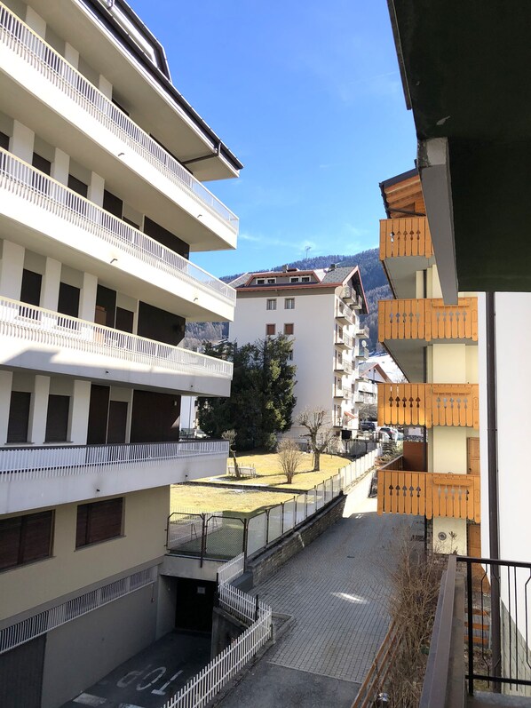 A multi-story building with balconies, a courtyard, and a mountain backdrop. - Maranta Master Guest apartment (Aprica)