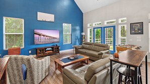 Un salon spacieux avec un mur d’accent bleu, un grand téléviseur à écran plat, une table de baby-foot et un coin salon confortable.