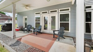 Un porche abrité avec deux fauteuils Adirondack, un barbecue et un tapis rouge.
