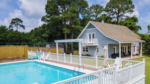 Une piscine résidentielle entourée d’une clôture blanche, un patio couvert et une maison dotée d’un balcon.