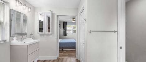 A narrow hallway with a white vanity, a mirror, and a bed in the background.