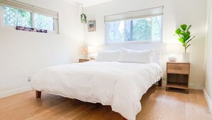 Una camera da letto con un letto grande, pavimento in legno, due comodini con lampade e una finestra vista alberi.