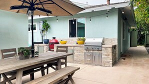 Patio esterno con tavolo e panche in legno, barbecue e una ghirlanda di luci.