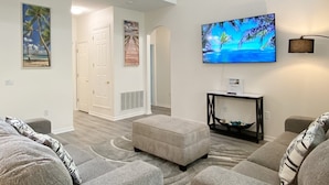 Un salón amplio con techos altos, un televisor de pantalla plana montado en la pared y una escalera que conduce a un nivel superior.