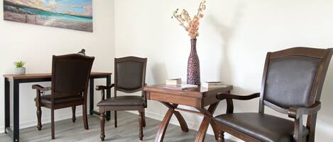 A room with a wooden desk, two chairs, a vase with flowers, and a painting on the wall.