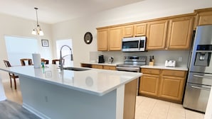 Una cocina moderna con una isla central, armarios de madera, electrodomésticos de acero inoxidable y un comedor con sillas.