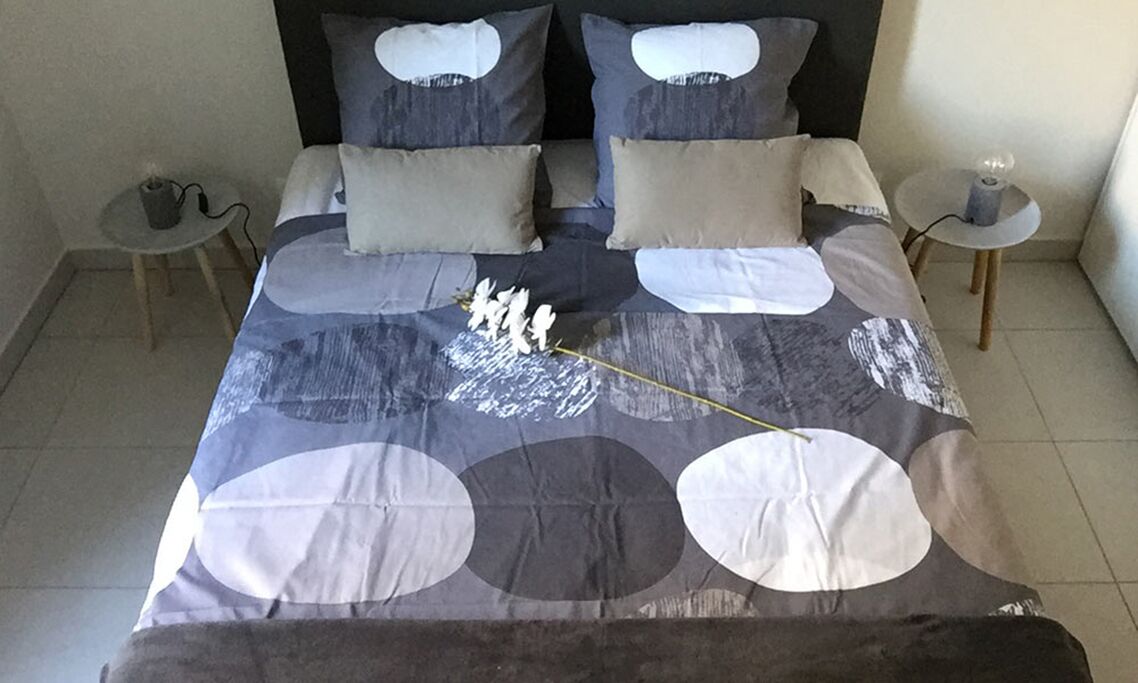 Ein ordentlich bezogenes Bett mit einem gemusterten Überwurf, zwei Nachttische mit Lampen und eine kleine Pflanze auf einem Tisch.