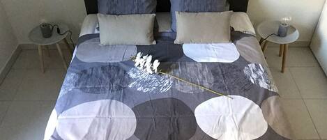 Ein ordentlich bezogenes Bett mit einem gemusterten Überwurf, zwei Nachttische mit Lampen und eine kleine Pflanze auf einem Tisch.