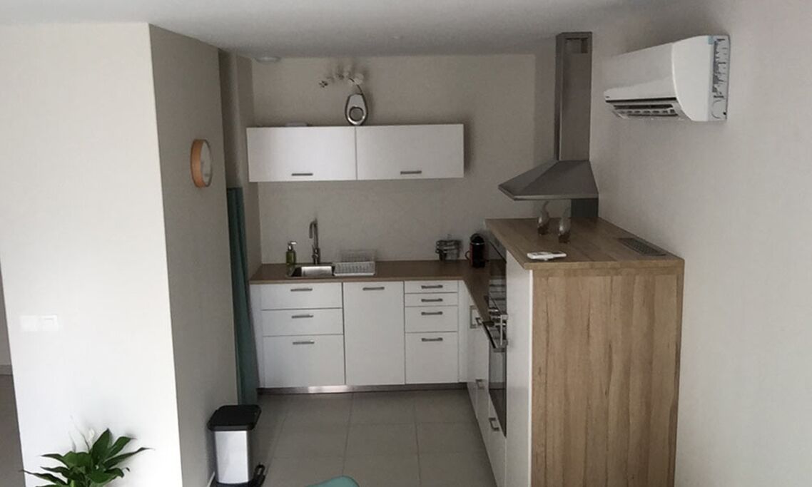 Eine kompakte Küche mit weißen Schränken, einer Holz Arbeitsplatte und einer Klimaanlage.