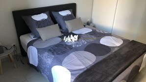A neatly made bed with a patterned bedspread, a bedside table with a lamp, and a wall-mounted nightstand.