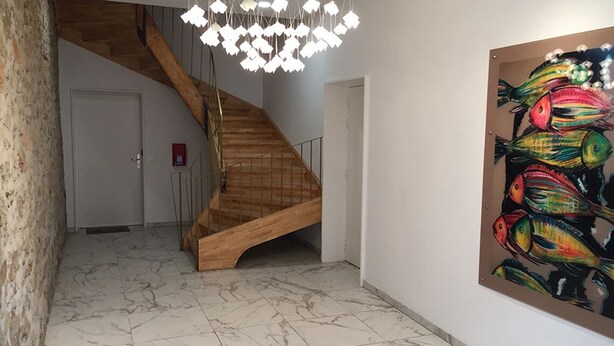 A wooden staircase with a modern chandelier, a marble floor, and a colorful fish painting on the wall.