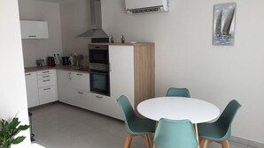 A modern kitchen with white cabinets, a built-in oven, and a dining area with a round table and teal chairs.