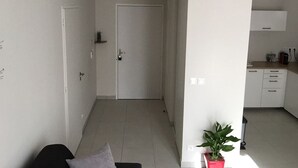 A modern, minimalistic living space with a neutral color palette, a visible door leading to a kitchen area, and a potted plant adding a touch of greenery.