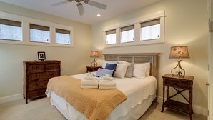 A bedroom with a large bed, two bedside tables with lamps, a wooden dresser, and a ceiling fan. - Cute little Cottage! Perfect Getaway! 2 Pools! SLEEPS 4 w/ BEACH CHAIRS! (Santa Rosa Beach)