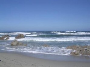 Une plage où les vagues se brisent contre les rochers, sous un ciel dégagé.