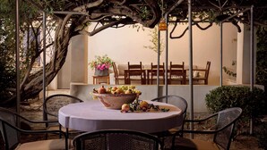 A round table with a bowl of fruit and a candle, surrounded by metal chairs, under a pergola with climbing plants. - Muazzo Historic Residence, a modernized gem (Pigi, Rethymno)