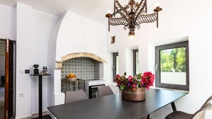 A modern kitchen with a built-in stove, a decorative fireplace, and a dining area with a large table and chairs. - Muazzo Historic Residence, a modernized gem (Pigi, Rethymno)