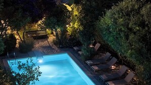 A rectangular swimming pool with lounge chairs and a bench, surrounded by trees and illuminated by ambient lighting. - Muazzo Historic Residence, a modernized gem (Pigi, Rethymno)