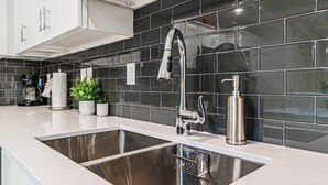 A modern kitchen with stainless steel sinks, a black tiled backsplash, and white cabinetry. - Spacious End-Unit Condo | Modern Open Floor Plan w/ Elegant Décor & Full Comfort | Minutes to Disney (Kissimmee)