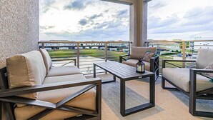 A balcony with outdoor seating, including a sofa and chairs, and a view of a building and landscape. - Spacious End-Unit Condo | Modern Open Floor Plan w/ Elegant Décor & Full Comfort | Minutes to Disney (Kissimmee)