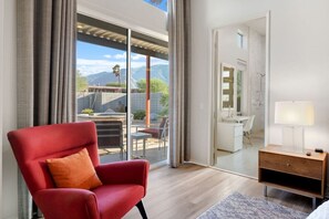 Habitació d'hotel moderna amb un gran finestral corredís que dona a un pati exterior, un sofà vermell, una tauleta de nit de fusta i un bany visible a través de la porta.