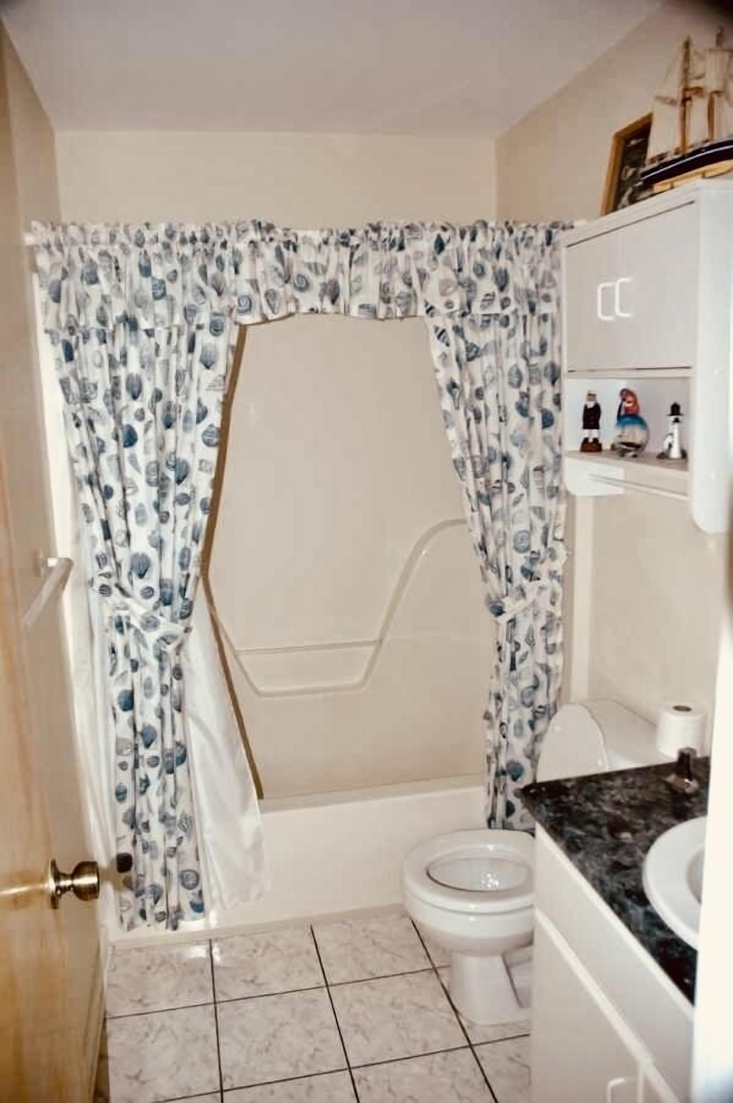 A bathroom with a shower curtain, toilet, and a vanity with a mirror.