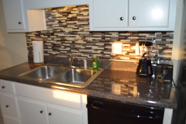 Cocina con encimera de granito, pileta de acero inoxidable y muebles altos blancos.