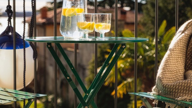 A glass table with a pitcher and glasses on a balcony, surrounded by greenery and a clear sky. - La Maison Du Lac Iseo - apt B (Predore)