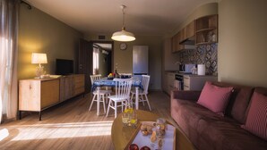 A living room with a brown sofa, a coffee table with snacks, and a dining area with a table and chairs. - La Maison Du Lac Iseo - apt B (Predore)