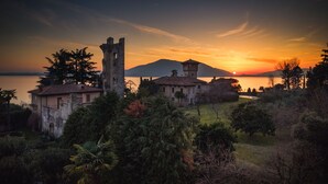 A historic building with a tower, surrounded by trees and overlooking a body of water at sunset. - La Maison Du Lac Iseo - apt B (Predore)