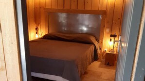 Une chambre aux murs lambrissés, avec un lit, deux tables de chevet et des lampes fixées au mur.
