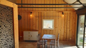 Un espace repas comprenant une table et des chaises, des murs en bois, une fenêtre et un plafond à structure quadrillée.
