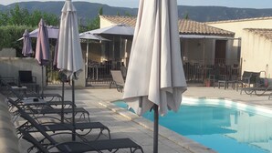 Un espace aménagé au bord de la piscine, avec des chaises longues et des parasols, une piscine et une vue sur des collines en arrière-plan.
