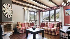 Una sala de estar acogedora con chimenea, dos sofás, una mesa de centro y ventanas amplias con vistas a las colinas.