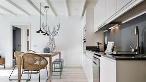 Una cocina moderna con armarios blancos, encimera negra y un comedor con sillas de mimbre.