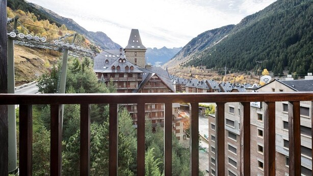 Un pueblo de montaña con un edificio destacado que tiene una torre, rodeado de exuberante vegetación y montañas.