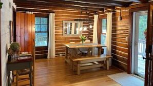 A rustic cabin interior with a wooden dining table, bench, and a small seating area. - Updated Vintage 1938 Log Cabin – Walk to Sister Bay (Sister Bay)