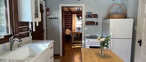 Una cocina con vigas de madera, armarios blancos, una mesa de comedor de madera y una lámpara colgante.