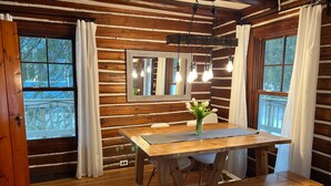 A wooden cabin interior with a dining table, chairs, a vase of flowers, and a hanging light fixture. - Updated Vintage 1938 Log Cabin – Walk to Sister Bay (Sister Bay)