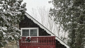 A log cabin with a stone foundation, a wooden deck, and a red balcony. - Updated Vintage 1938 Log Cabin – Walk to Sister Bay (Sister Bay)