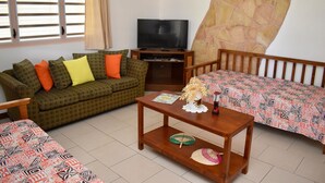 A living room with a sofa, a coffee table, a television, and a patterned bedspread. - Aito1 across from Muri Beach (Muri Beach)