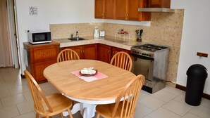 A kitchen with wooden cabinets, a stove, a microwave, and a dining table with chairs. - Aito1 across from Muri Beach (Muri Beach)