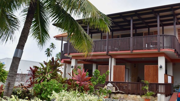 A two-story building with a balcony, surrounded by tropical plants and palm trees. - Aito1 across from Muri Beach (Muri Beach)